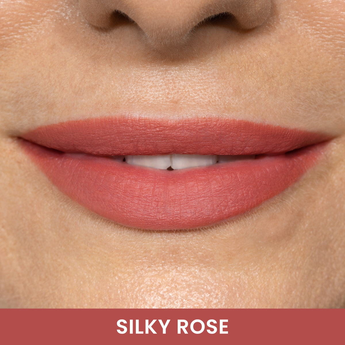 Close-up of a persons smiling lips wearing a matte rosy pink lipstick. The label below reads SILKY ROSE in white text on a rose-colored background.