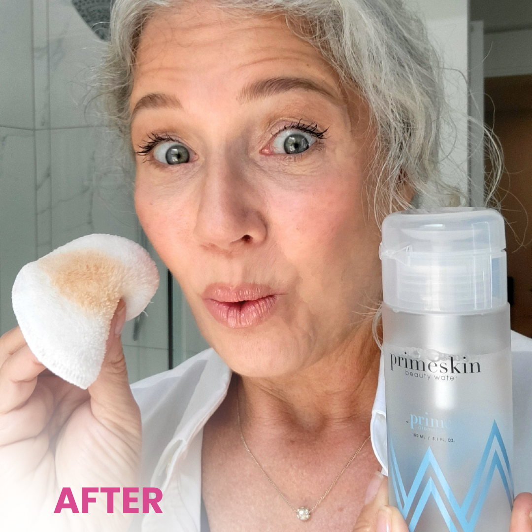A woman with gray hair holds a cotton pad with makeup residue in one hand and a bottle of Primeskin Beauty Water in the other. She looks surprised and stands in a bright bathroom. The word AFTER appears in pink text.