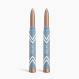 Two light brown, shimmery 2pcs PrimeEyes Eye Brightener sticks from PrimePrometics™ stand side by side in blue and white chevron tubes labeled "prime"—ideal for effortless eye brightening and care against a white background.