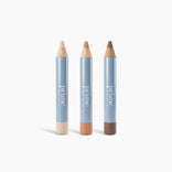 Three thick creamy PrimePrometics™ Full-Face Concealer Set pencils stand upright against a white background, each in light beige, medium tan, or deep brown—ideal for concealing dark circles on mature skin.