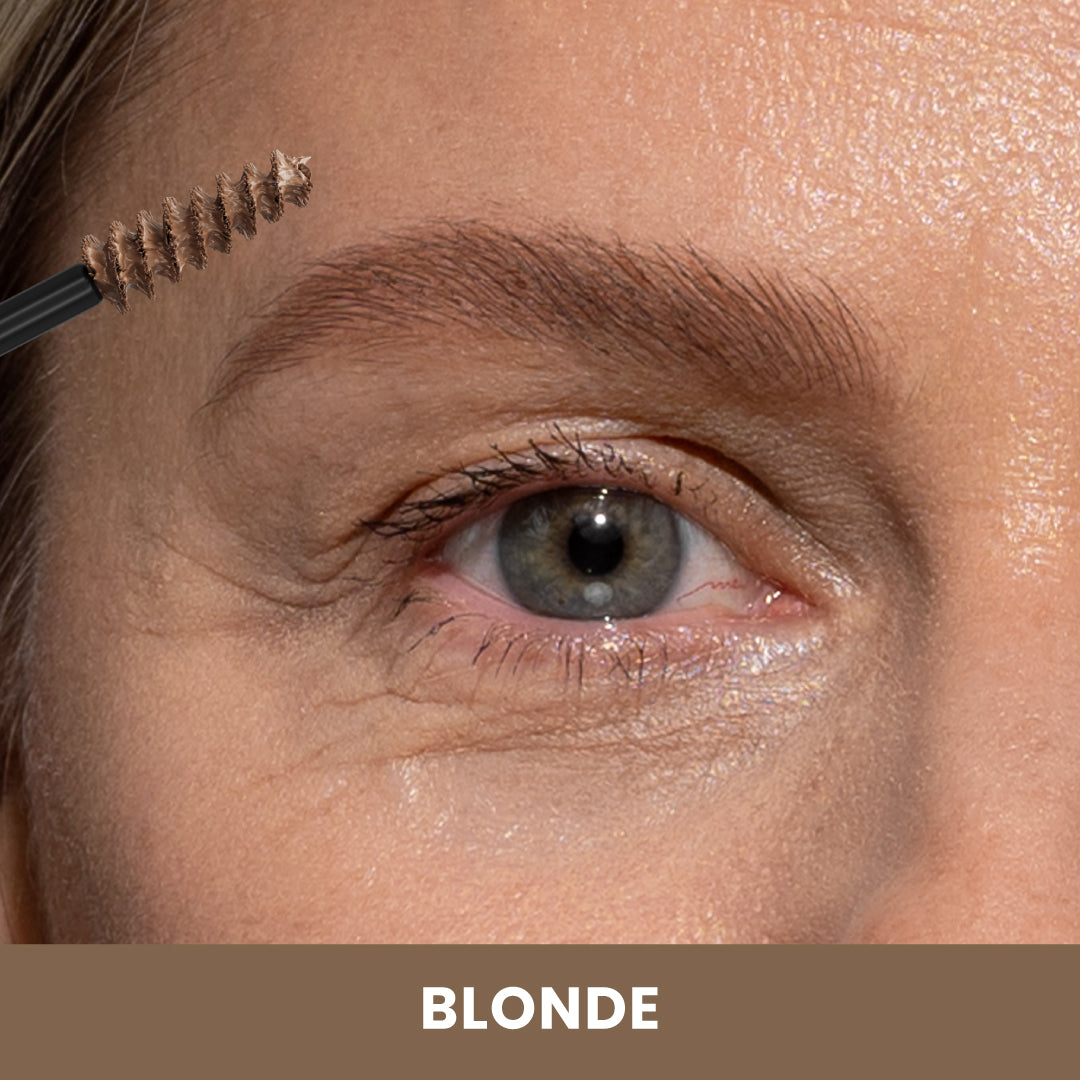 A close-up of a persons eye and eyebrow as a spoolie brush with blonde eyebrow product is applied. The image has the label BLONDE at the bottom.