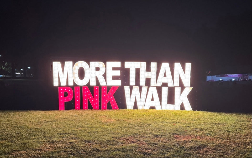 Large illuminated sign reading “MORE THAN PINK WALK” with the words “PINK WALK” in bright pink lights, displayed outdoors on grass at night.