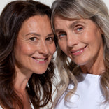 Two mature women smiling side by side with visibly defined brows