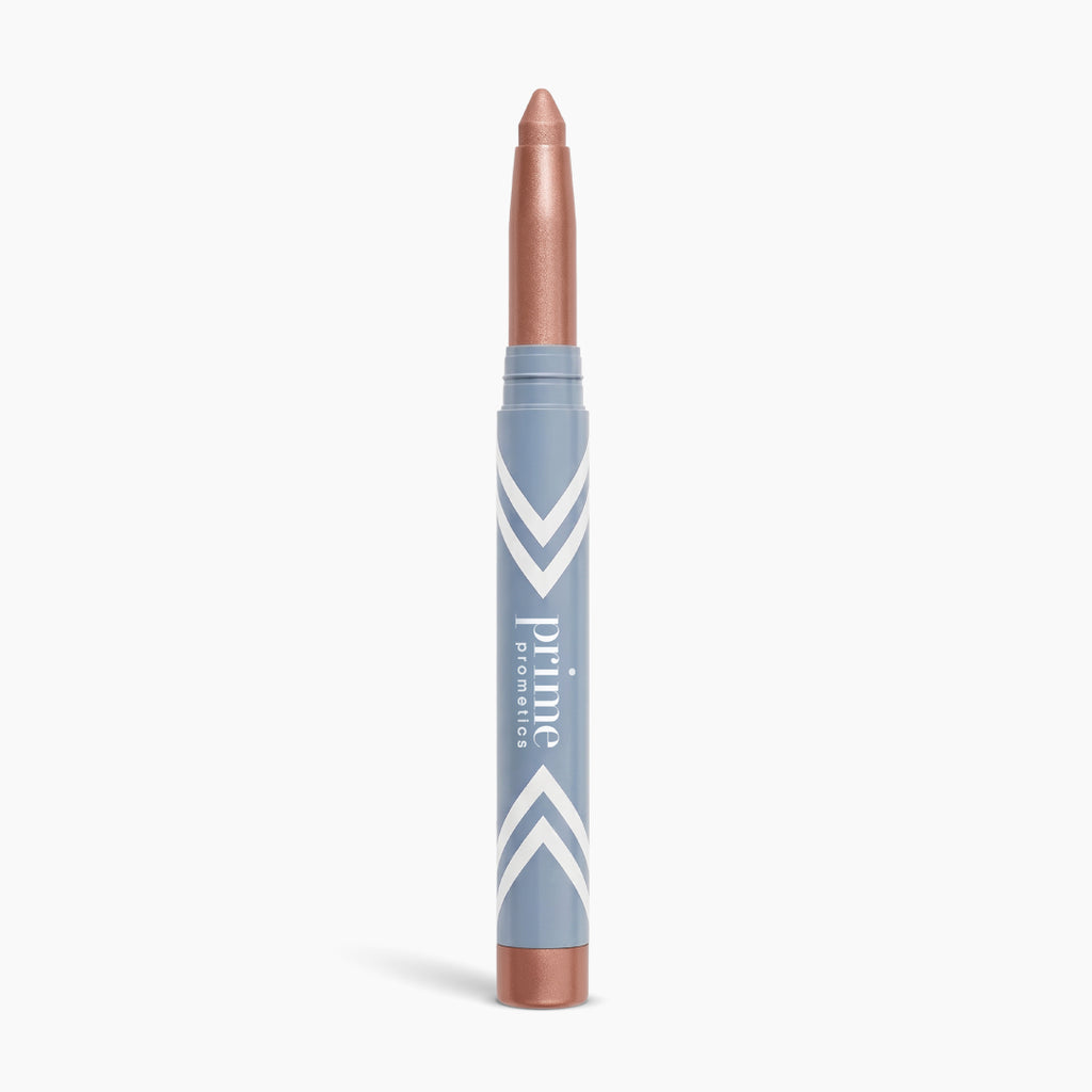 A metallic rose gold illuminating eyeshadow stick, the PrimeEyes Eye Brightener by PrimePrometics™, stands upright against a white background in its sleek blue and white tube—perfect for creating an effortless eye lift effect.