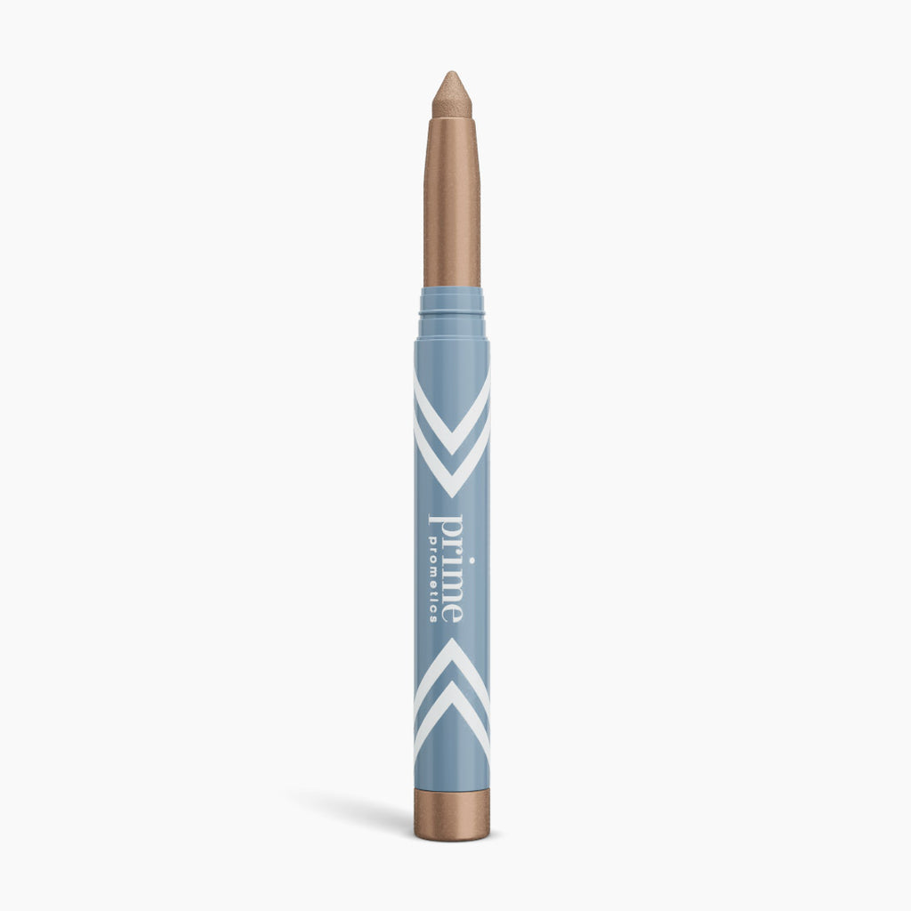 The PrimePrometics™ PrimeEyes Eye Brightener is a blue and gold makeup crayon with white chevrons and "prime promise" text, offering illuminating eyeshadow and eye lift effects for women over 50. It stands upright on a white background.