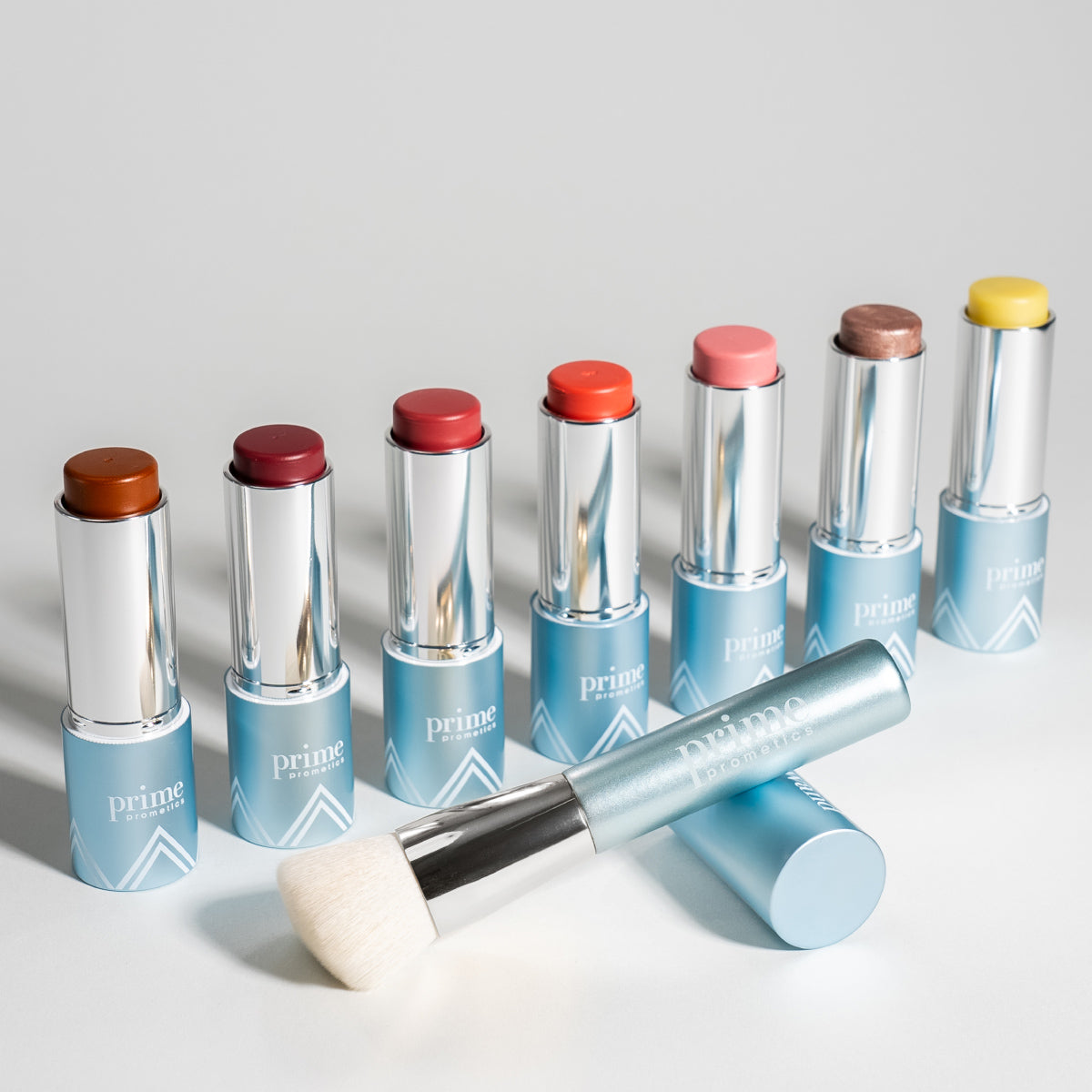 PrimeWand Brush displayed alongside the Prime Prometics PrimeWand color stick family in eight shades for cheeks and lips