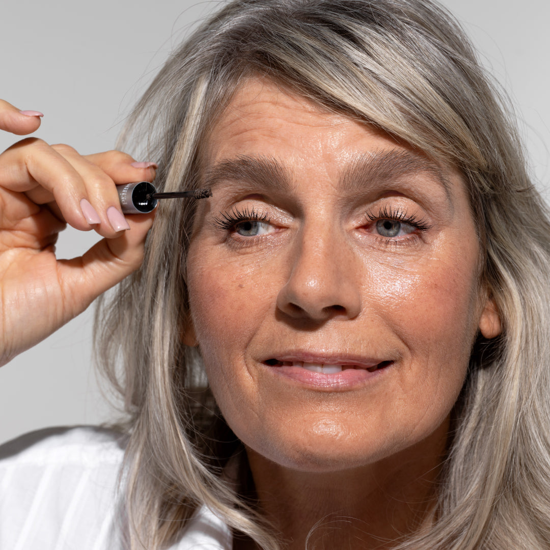 Mature woman applying Prime Prometics PrimeBrow Tinted Gel to her brow with the spoolie wand