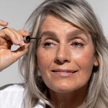Mature woman applying Prime Prometics PrimeBrow Tinted Gel to her brow with the spoolie wand