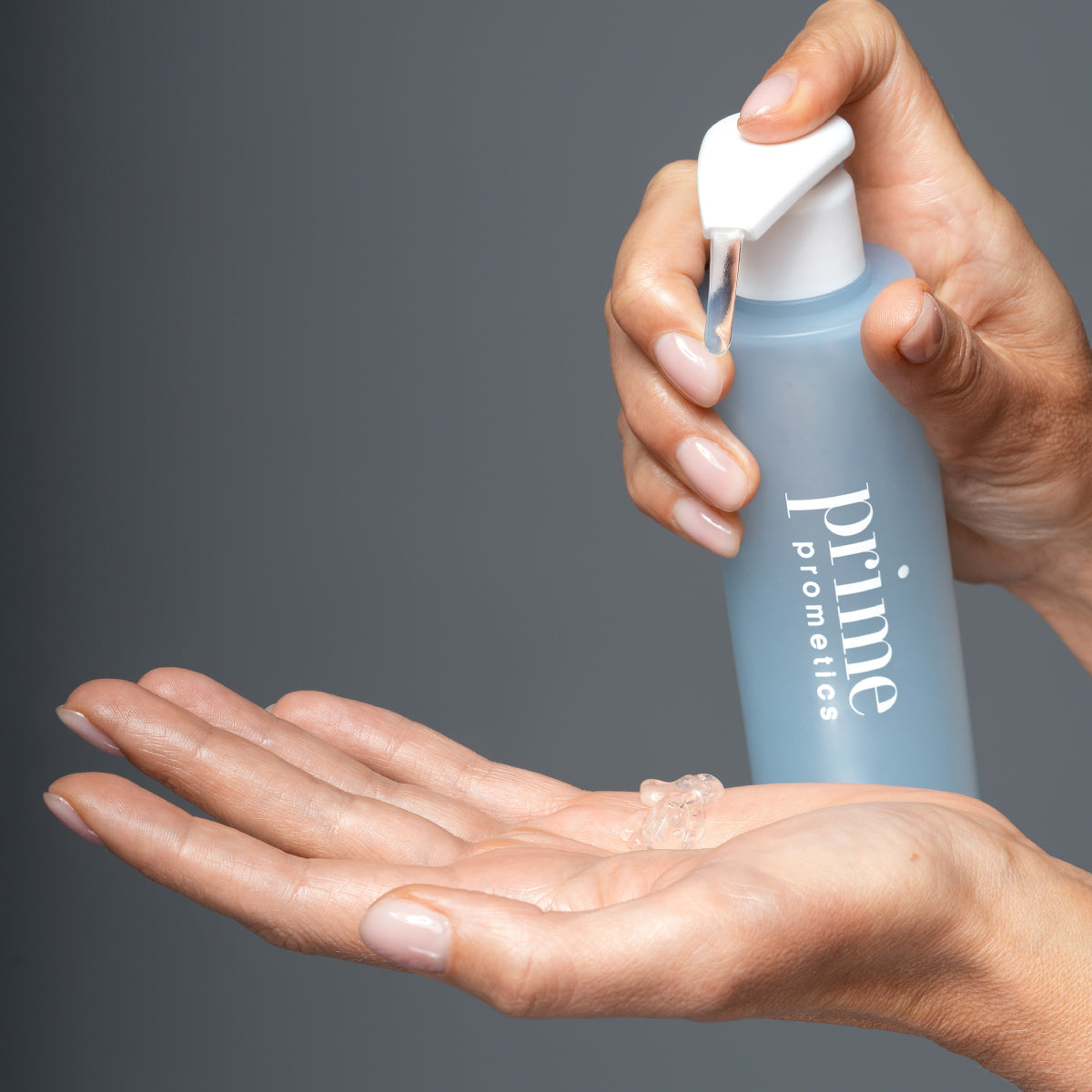 A person dispenses a clear gel from a blue bottle labeled prime prometics onto their open palm against a plain gray background.