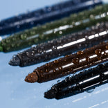Five PrimePrometics™ eyeliner pencils in black, brown, gray, green, and blue—each with water droplets—are arranged diagonally on a reflective light blue surface. Create your perfect Build Your Own Bundle of eye essentials.