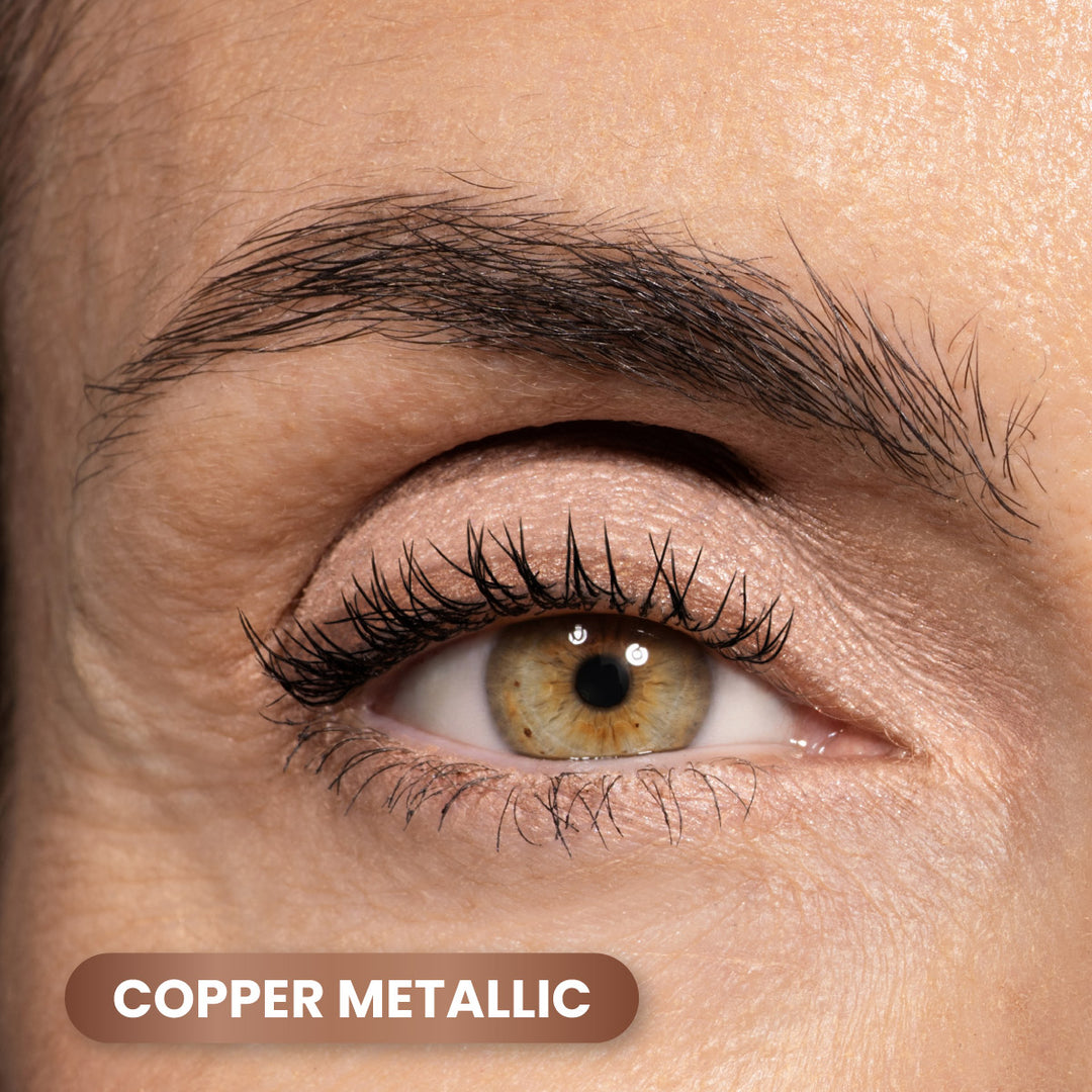 Close-up of a persons eye with copper metallic eyeshadow on the eyelid. The person has brown eyes, long eyelashes, and well-groomed eyebrows. The text COPPER METALLIC appears at the bottom left.