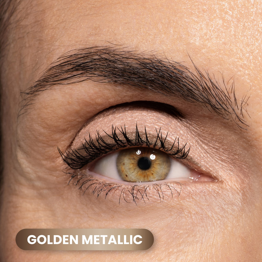 A close-up of a persons eye with gold metallic eyeshadow on the eyelid. The eyebrow is well-groomed, and the eyelashes are long. A label at the bottom left reads GOLDEN METALLIC.