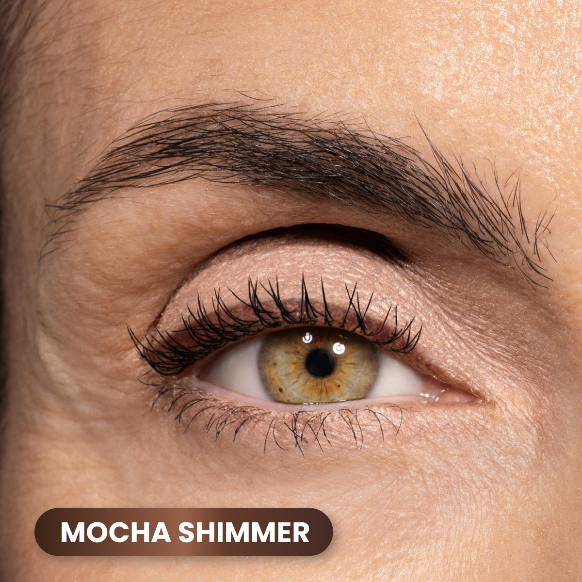 A close-up of a persons eye with light brown shimmery eyeshadow on the eyelid. The eyebrow is neatly groomed. A label in the corner reads Mocha Shimmer.