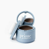 An open PrimePrometics™ Instant Coverage Hairline Powder in a blue container with built-in mirror and applicator reveals brown powder for gray root coverage, set against a plain white background.