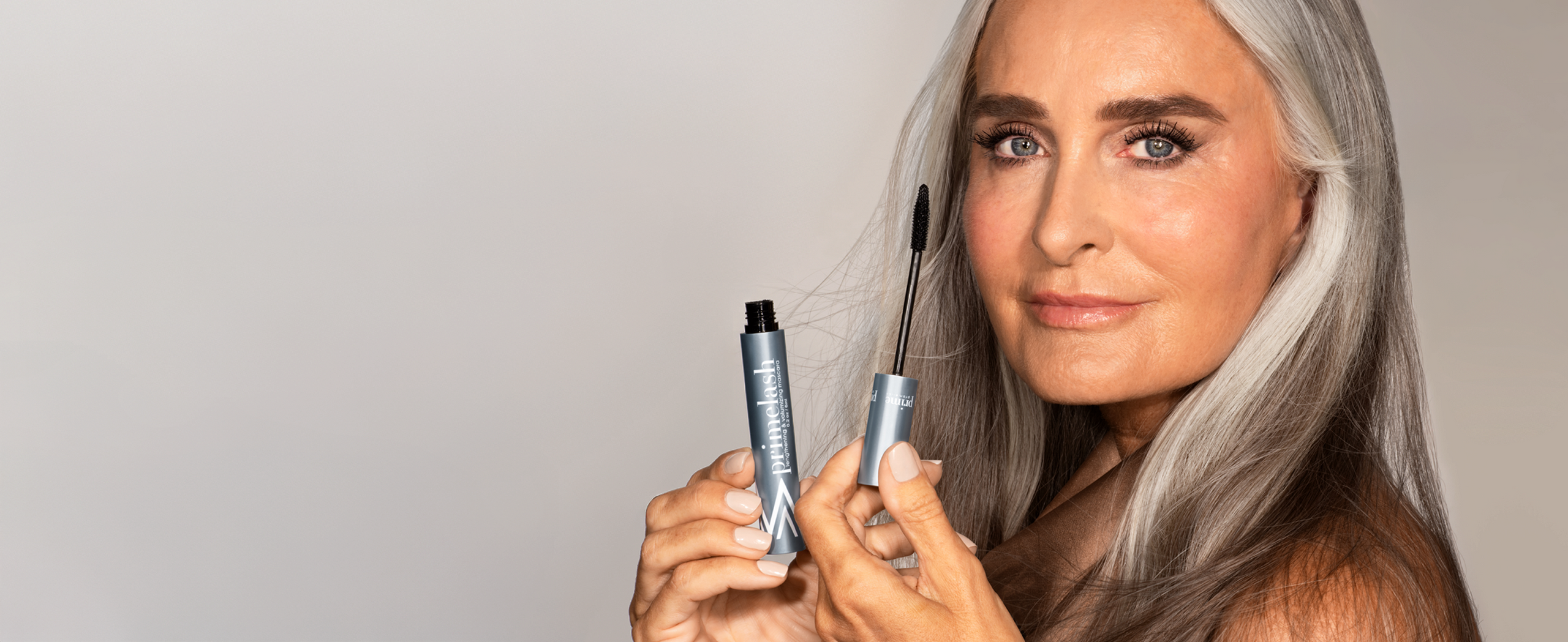 Mature woman with grey hair applying Prime Prometics pro-age mascara.