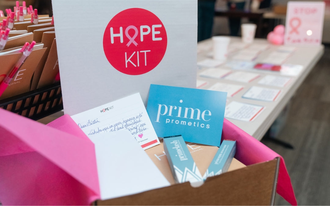A box labeled HOPE KIT contains a handwritten note, Prime Prometics cards, and beauty products. In the background, a table displays informational cards and pink pens, suggesting a breast cancer awareness event.