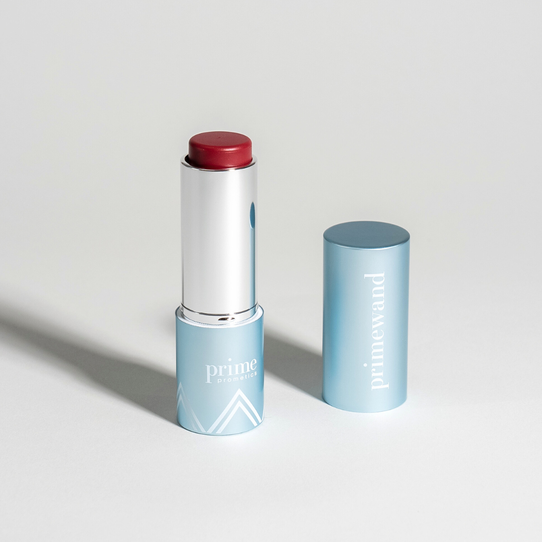 A red lipstick in a light blue tube labeled prime promise stands upright with its matching cap, labeled primewand, placed next to it on a white background.