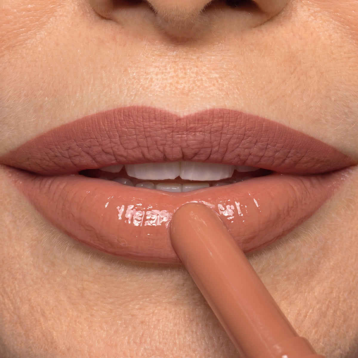 Close-up of a person applying nude lipstick to their lips, which are already covered with a matte lip color. Teeth are slightly visible and skin texture is detailed.