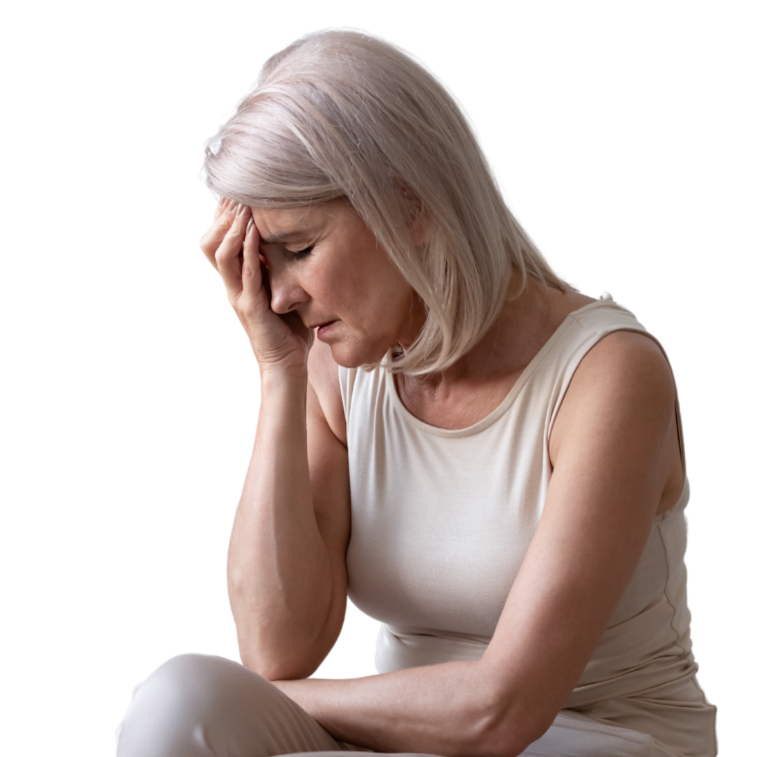 Older woman with light hair sits and holds her head in her hand, eyes closed, appearing stressed, tired, or in pain, against a plain white background.