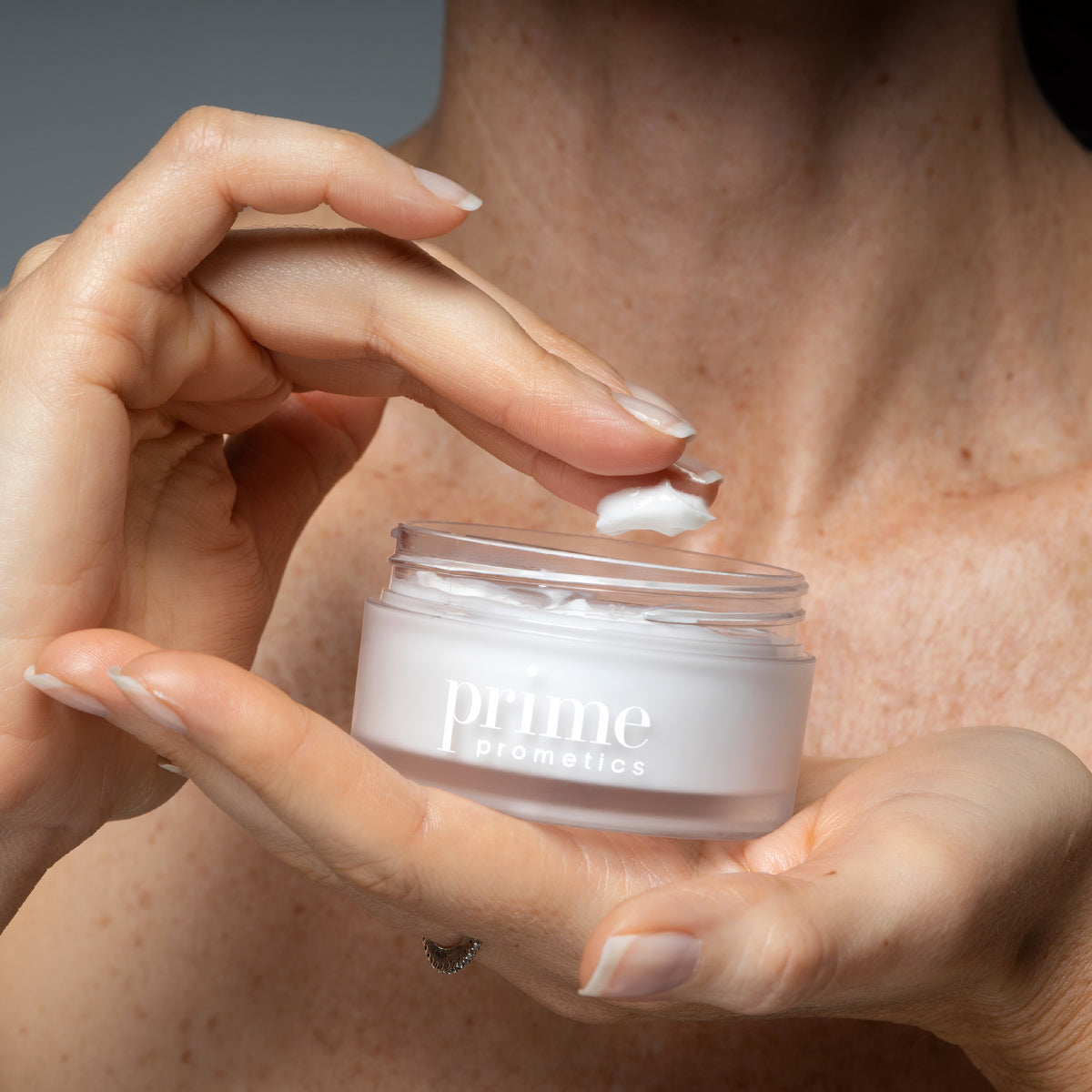 Mature woman scooping Prime Prometics Miracle Cream from its open jar with her index finger
