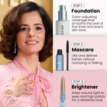 A woman with curled brown hair and pink lipstick wears a pink blouse and earrings. Beside her, the PrimePrometics™ Hollywood Glow Set shows Foundation, Mascara, and Brightener for smooth, defined, and refreshed looks.