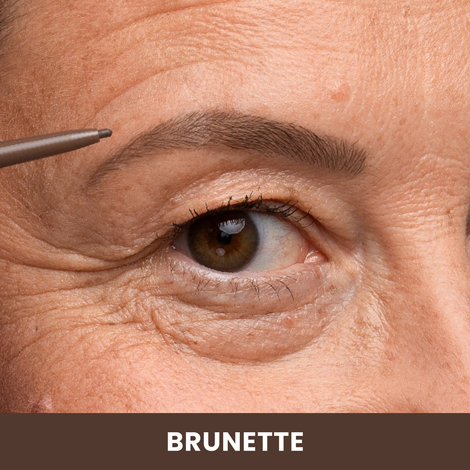 A close-up of a persons eye and eyebrow as they fill in their brow with a brown pencil. The skin shows natural texture, and the caption below reads BRUNETTE.