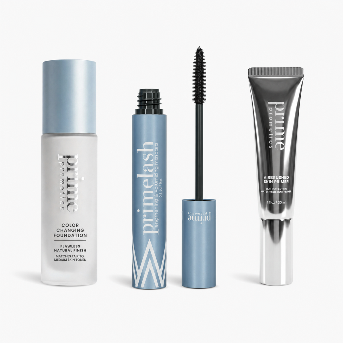 Das PrimePrometics™ Prime Perfection Trio – bestehend aus der Color Changing Foundation, der PrimeLash Mascara (abgebildet mit sichtbarem Applikator) und dem Airbrushed Skin Primer – steht aufrecht in einer eleganten blau-silbernen Verpackung vor einem weißen Hintergrund.