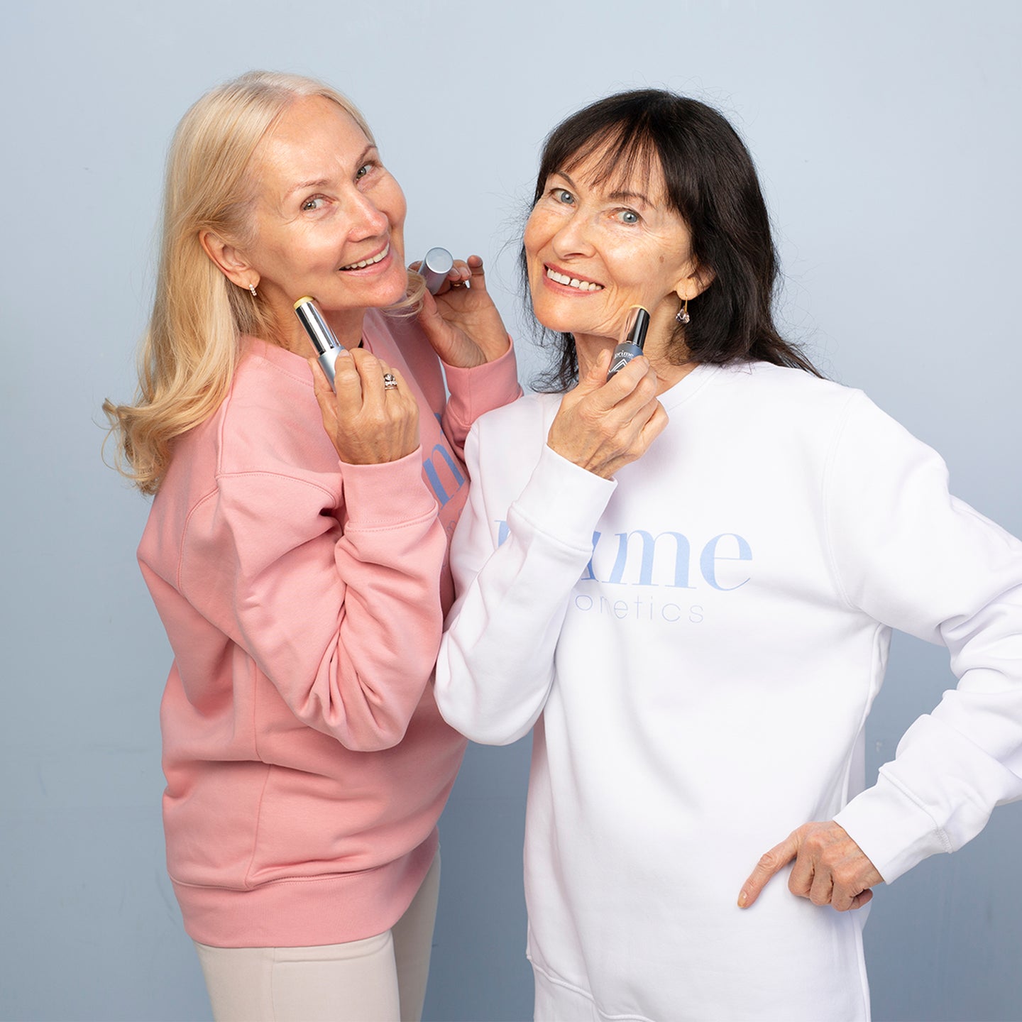 Two women over 50 smiling and applying Prime Prometics PrimeWand Nourish moisturizer sticks to their cheeks