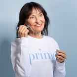 Mature woman with dark hair smiling and applying Prime Prometics PrimeWand Pigment to her cheek