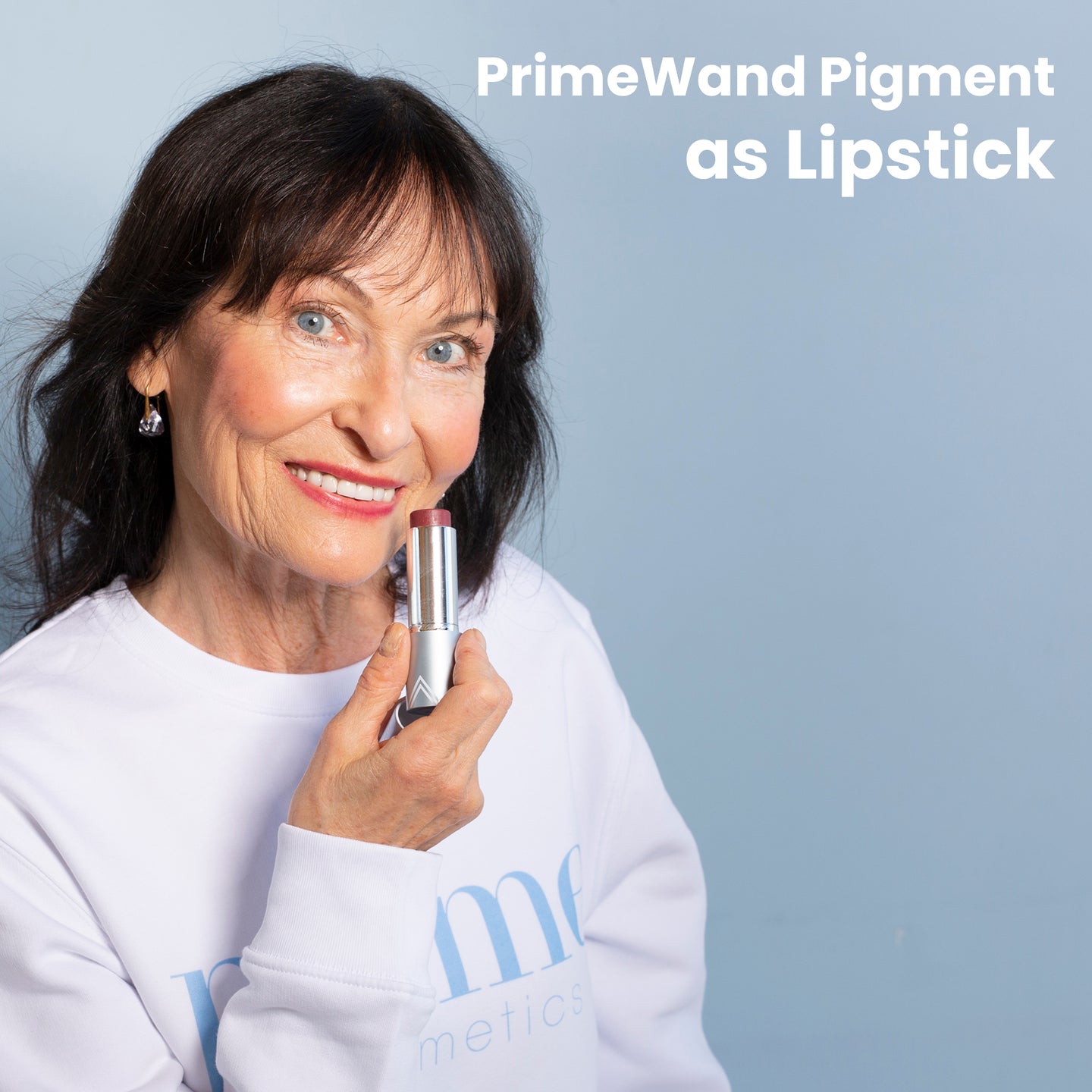 PrimeWand Pigment as Lipstick: a mature woman with dark hair holding the Prime Prometics PrimeWand Pigment stick near her berry-tinted lips