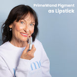 PrimeWand Pigment as Lipstick: a mature woman with dark hair holding the Prime Prometics PrimeWand Pigment stick near her berry-tinted lips