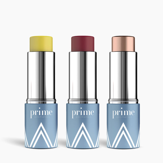 Three PrimePrometics™ PrimeWand Trinity sticks stand upright, each in a silver case with a blue base and white geometric design, showing multitasking shades: yellow, deep red, and shimmery beige.