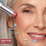 A smiling woman applies PrimePrometics™ PrimeWands 5-in-1 Makeup Wand in a nude cream blush shade to her cheek. Instructions read: CHEEKS: Blend over cheeks for a soft, natural-looking flush of buildable color. LIPS: Swipe on for polished everyday rosy-nude color.