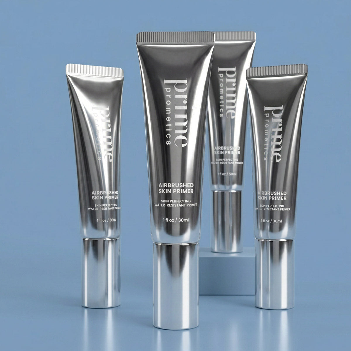 Four metallic silver tubes of Prime Prometics Airbrushed Skin Primer stand upright on a blue surface, with product labels visible. The tubes are arranged at varying angles and distances.