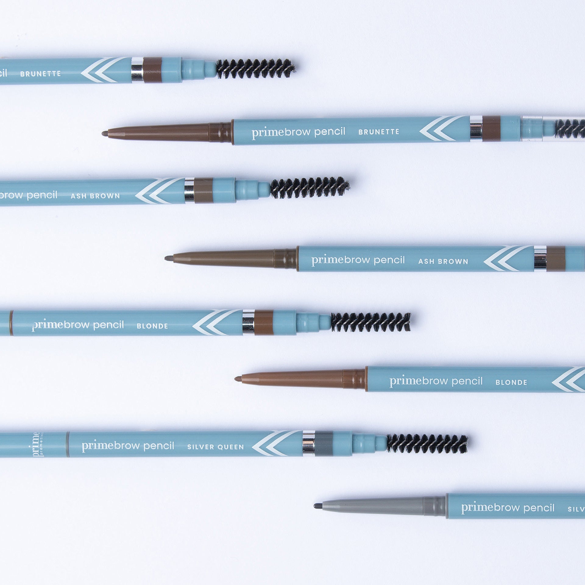 Several blue primebrow pencil eyebrow pencils are arranged diagonally on a white background, with visible shades labeled Brunette, Ash Brown, Blonde, and Silver Queen. Each pencil has a spoolie brush.