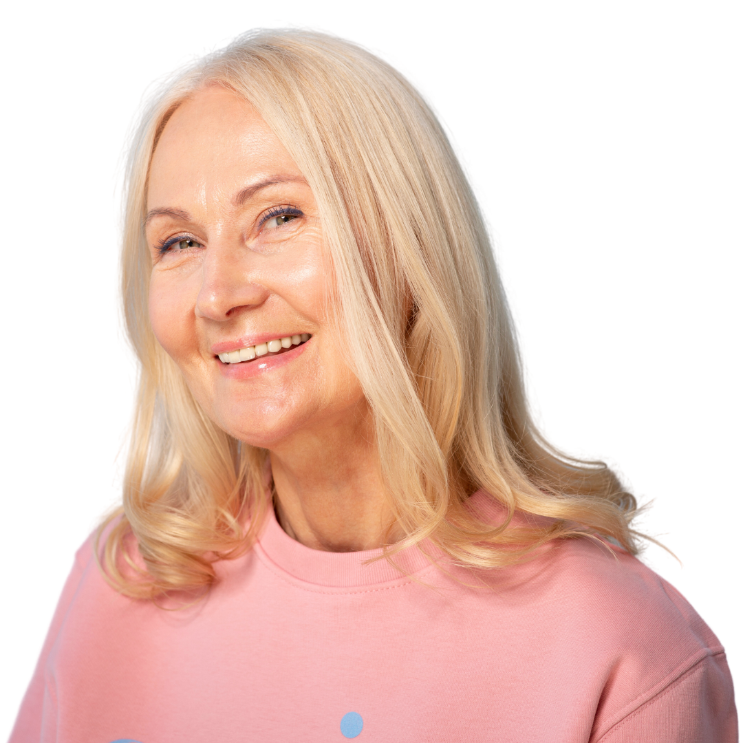 Smiling older woman with long blonde hair, wearing a light pink sweatshirt, poses against a plain white background.