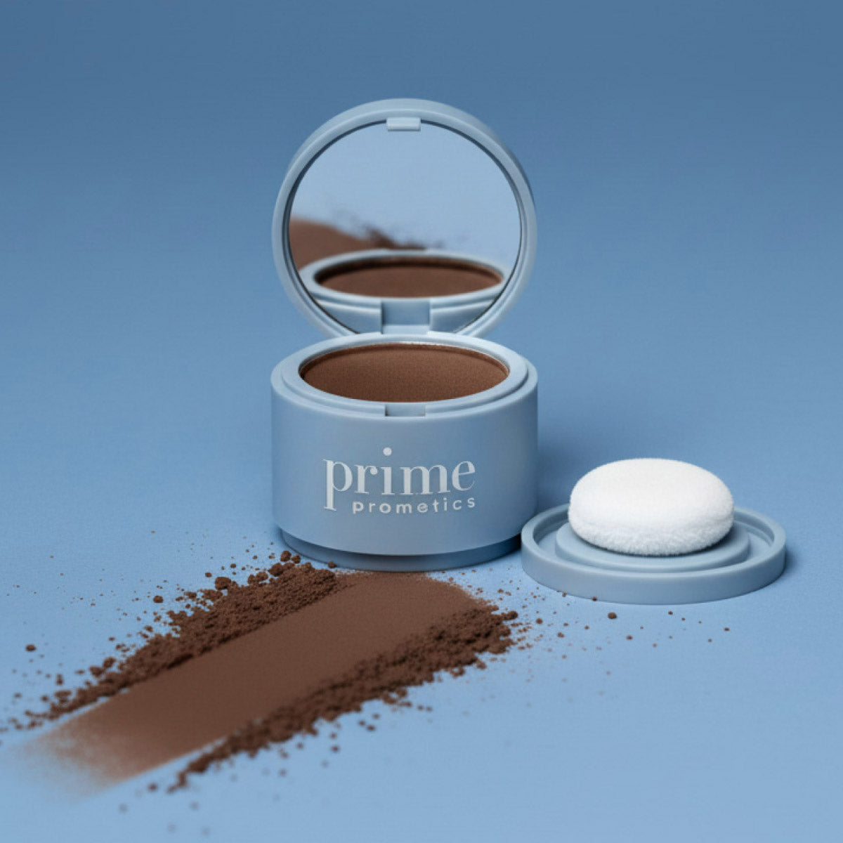A blue container of Prime Prometics cosmetic powder sits open with a mirror, showing brown powder inside. The powder is spread on the blue surface, alongside a white application puff and the container lid.