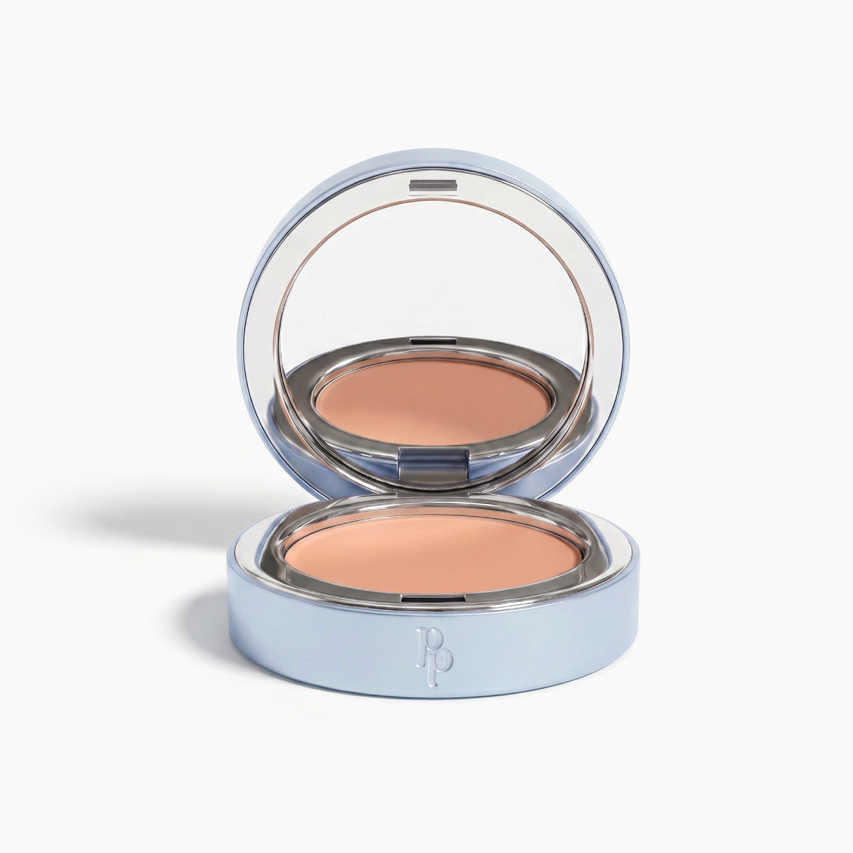 A sleek silver compact with mirror reveals a beige pressed powder foundation. The front features RP initials and pairs perfectly with PrimePrometics™ Undereye Brightening Corrector to visibly diminish dark circles.