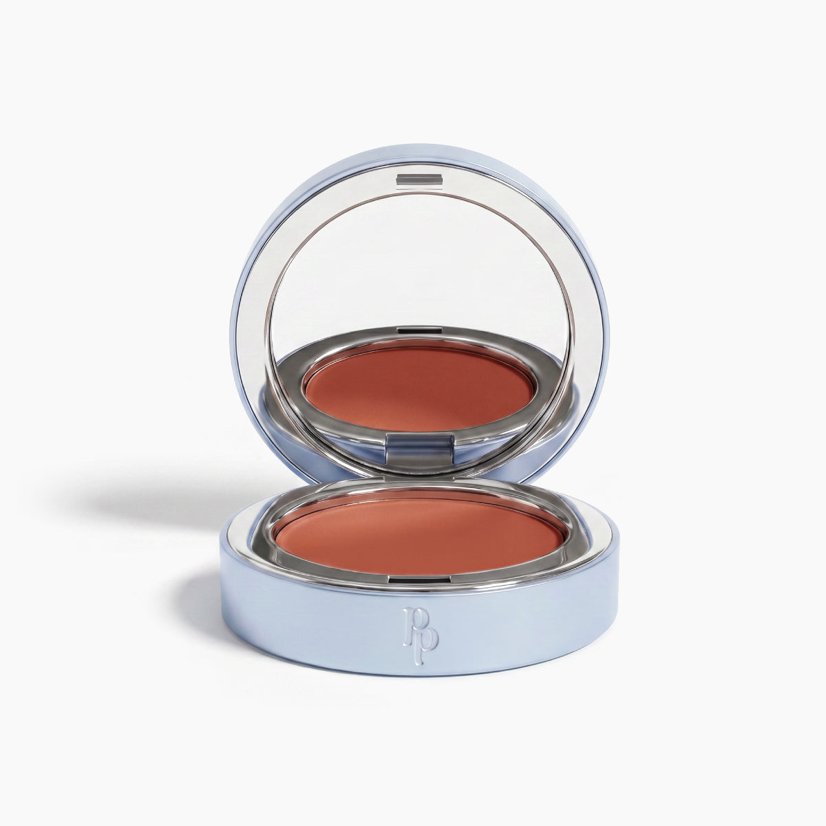 The PrimePrometics™ Undereye Brightening Corrector comes in a circular silver case with a mirror and embossed initials, revealing a warm terracotta shade perfect for targeting dark circles.