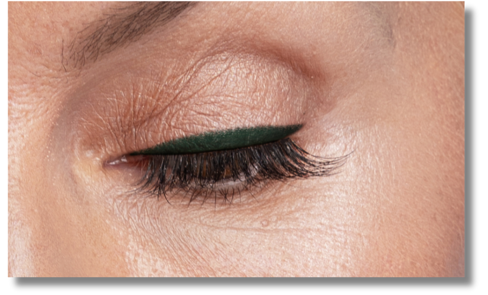 A close-up of a closed eye with winged dark green eyeliner and long eyelashes, showing smooth skin and natural eyebrow detail.
