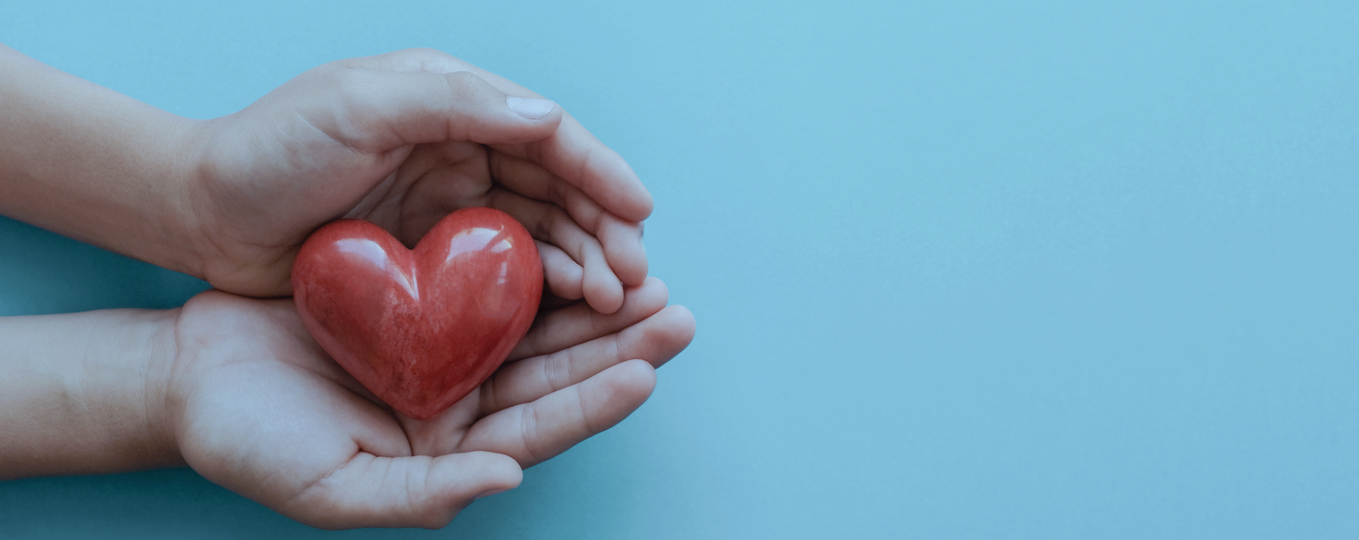 A pair of hands gently holding a red heart-shaped object against a light blue background, symbolizing care, love, and support.