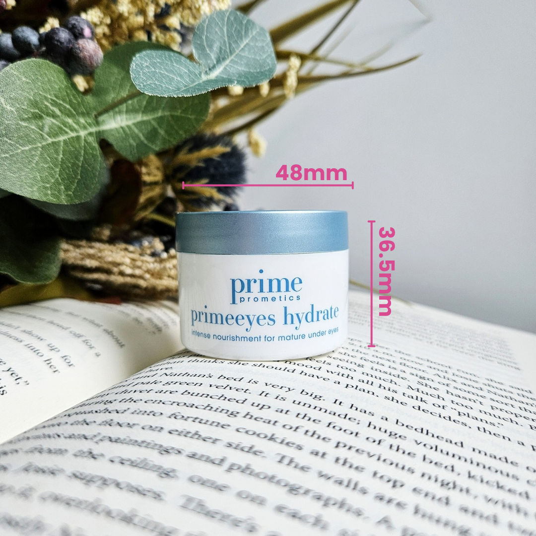 A small jar of prime cosmetics primeeyes hydrate cream sits on an open book, with labeled dimensions of 48mm width and 36.5mm height. In the background, eucalyptus leaves and dried flowers are visible.