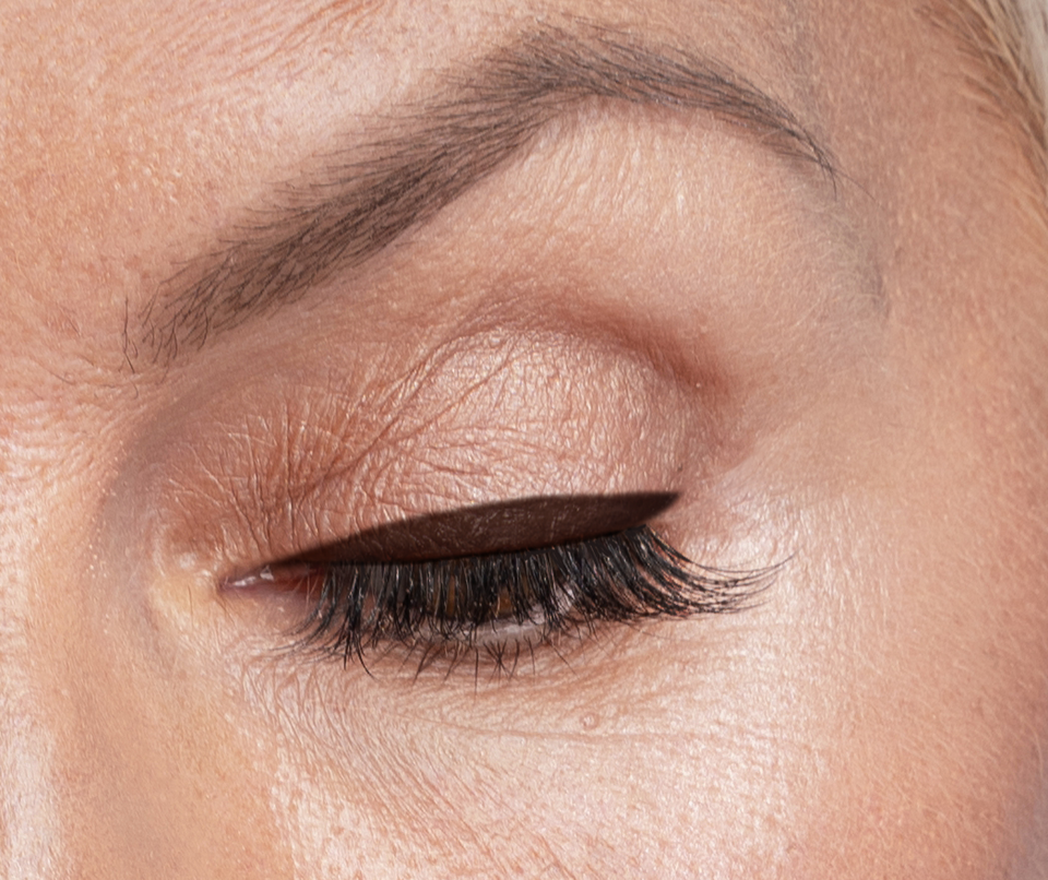 A close-up of a closed eye with well-groomed eyebrow, smooth skin, black eyeliner, and long, curled eyelashes.
