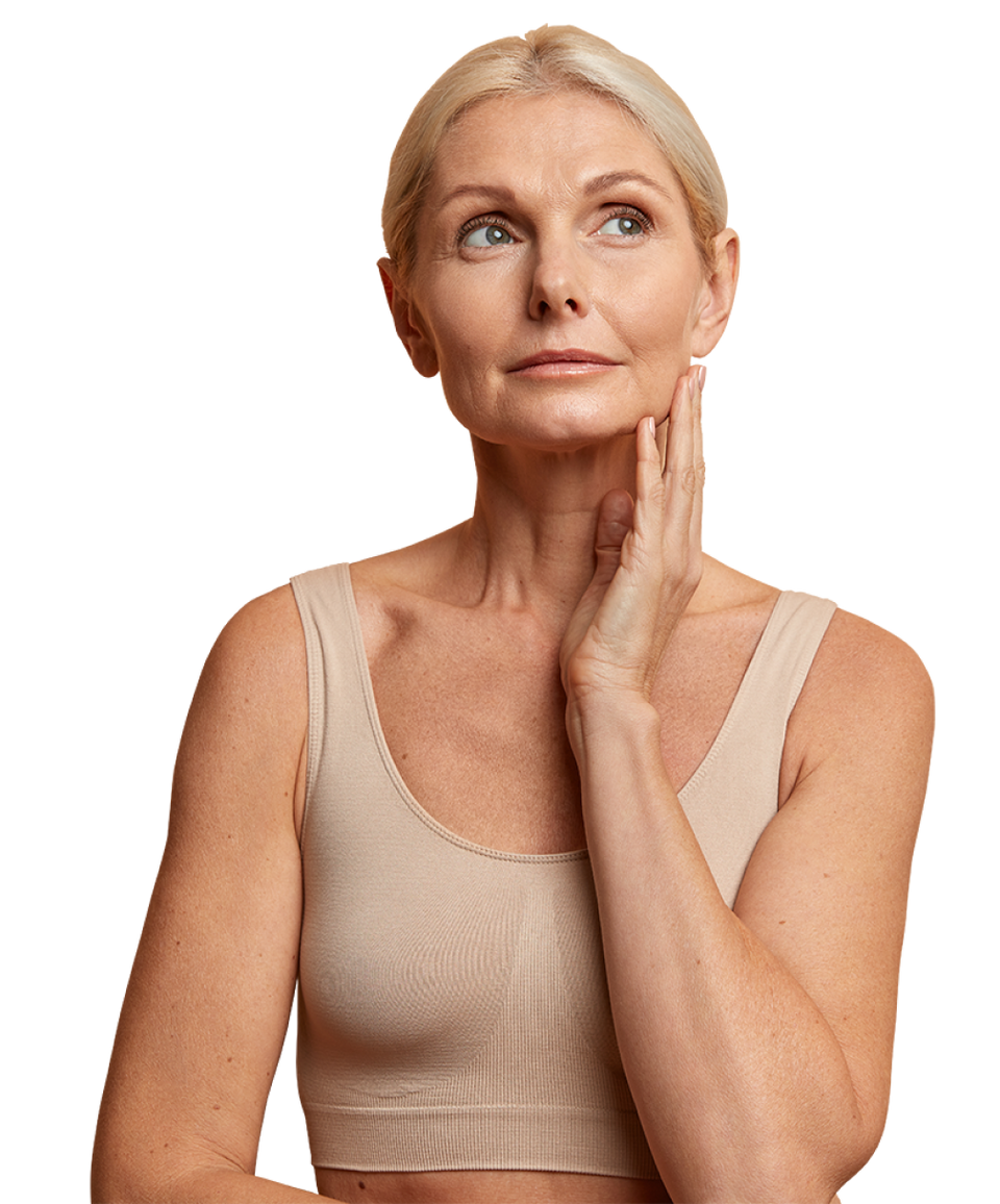 A woman with blonde hair in a bun, wearing a beige sleeveless top, looks upward thoughtfully while gently touching her face with one hand against a plain background.