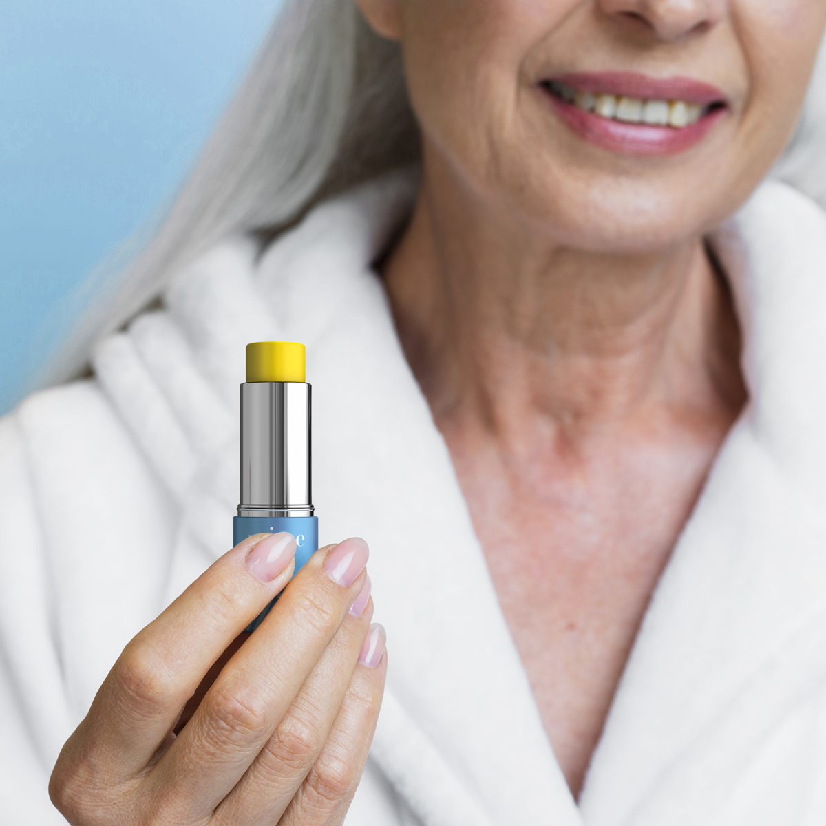 Older woman with white hair in a white robe holding the Prime Prometics PrimeWand Nourish moisturizer stick
