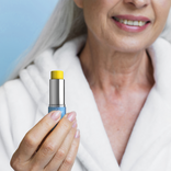 Older woman with white hair in a white robe holding the Prime Prometics PrimeWand Nourish moisturizer stick