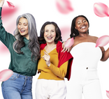 Three women of different ages and ethnicities smiling and posing together among falling pink rose petals